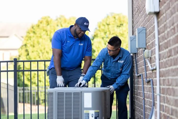 Two service technicians inspecting an outdoor air conditioning condenser