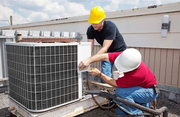 Two HVAC installers working together on an outdoor unit